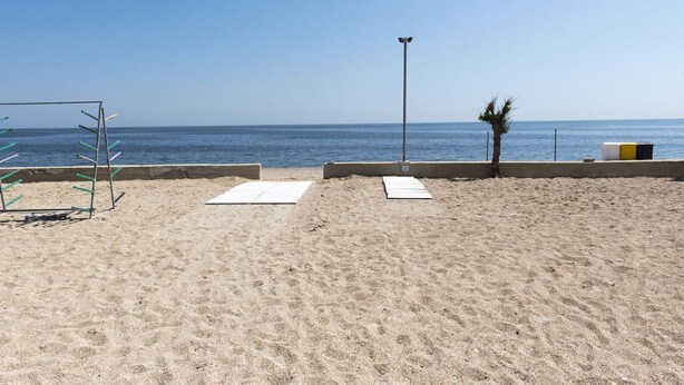 Ein sandiger Strand mit einer Metallkonstruktion, einer Straßenlaterne und einer Palme.