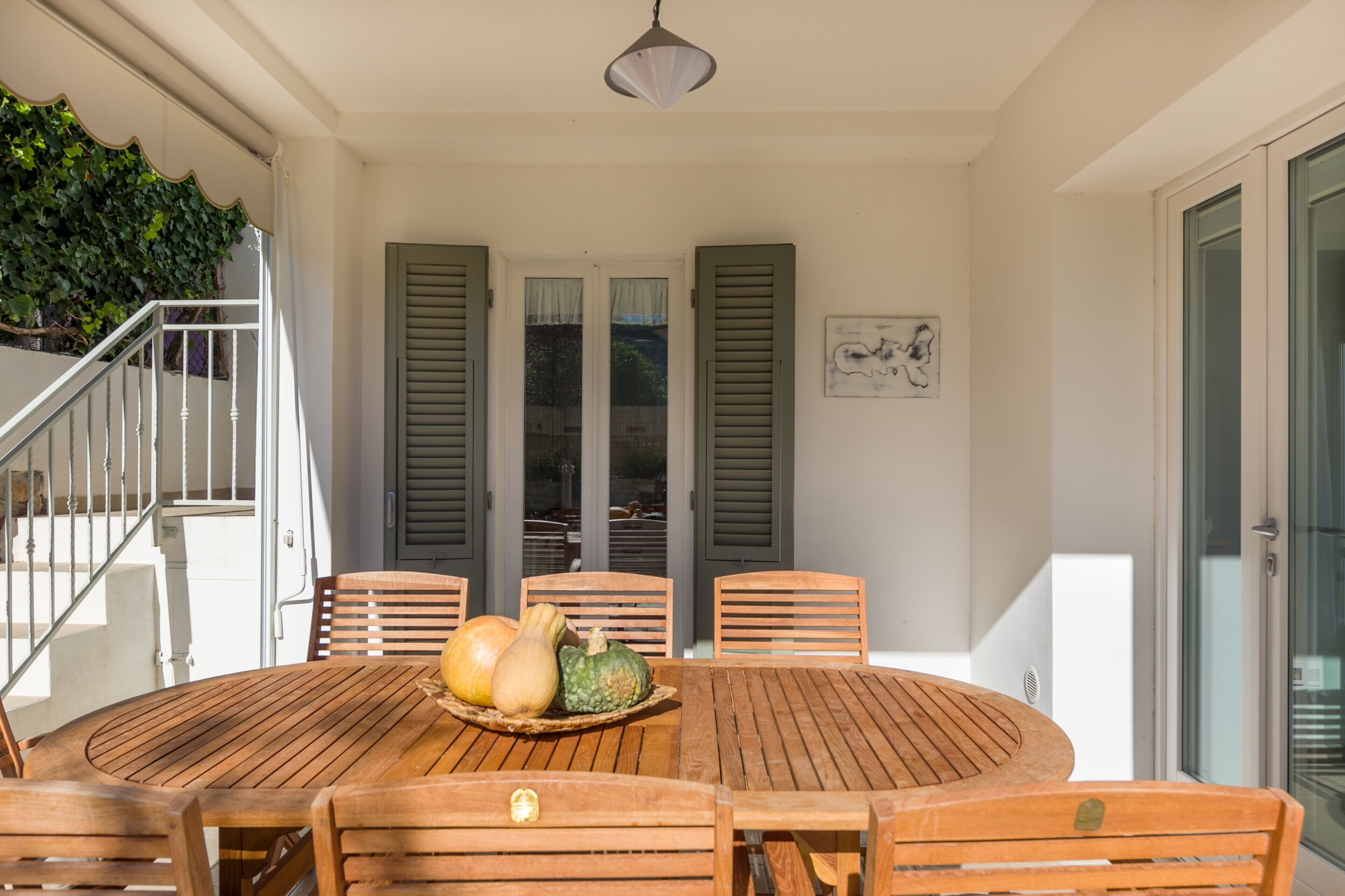 Un tavolo di legno con sedie, un cesto di verdure e una scala che conduce a un balcone.