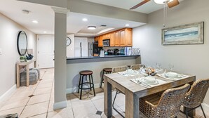 A modern kitchen with wooden cabinets, a dining area with a wooden table and wicker chairs, and a ceiling fan. - Beachy Marco Island Condo with Resort Amenities! (Marco Island)
