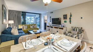 A modern living room with a dining area, a ceiling fan, and a television. - Beachy Marco Island Condo with Resort Amenities! (Marco Island)
