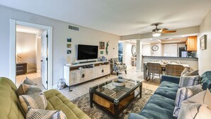 A spacious living room with a sofa, a coffee table, and a TV. There is a dining area with a table and chairs. The kitchen is visible in the background. - Beachy Marco Island Condo with Resort Amenities! (Marco Island)