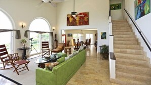 A spacious living room with a green sofa, wooden chairs, a dining area, and a staircase. - Villa Cielo Azul (Sardinal)