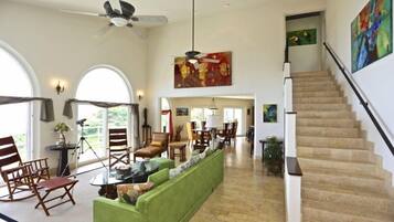A spacious living room with a green sofa, wooden chairs, a dining area, and a staircase.