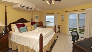 A bedroom with a bed, a ceiling fan, an air conditioning unit, a desk, a chair, and a view of the ocean through a sliding glass door. - Villa Cielo Azul (Sardinal)