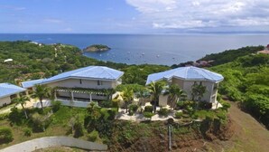 A coastal property with three houses, each with a blue roof, surrounded by lush greenery and a view of the sea with boats. - Villa Cielo Azul (Sardinal)