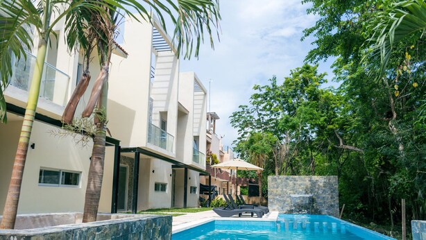 A modern pool area with a clear blue pool, surrounded by palm trees and a stone wall.