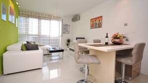 A modern living room with a white sofa, a dining area with a bar, and a kitchen in the background. - Apartment Antea (Split)