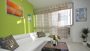 A modern living room with a white sofa, a coffee table with a vase of flowers, and a painting on the wall. - Apartment Antea (Split)