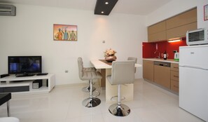 A modern kitchen with a dining area, a TV, and a painting on the wall.