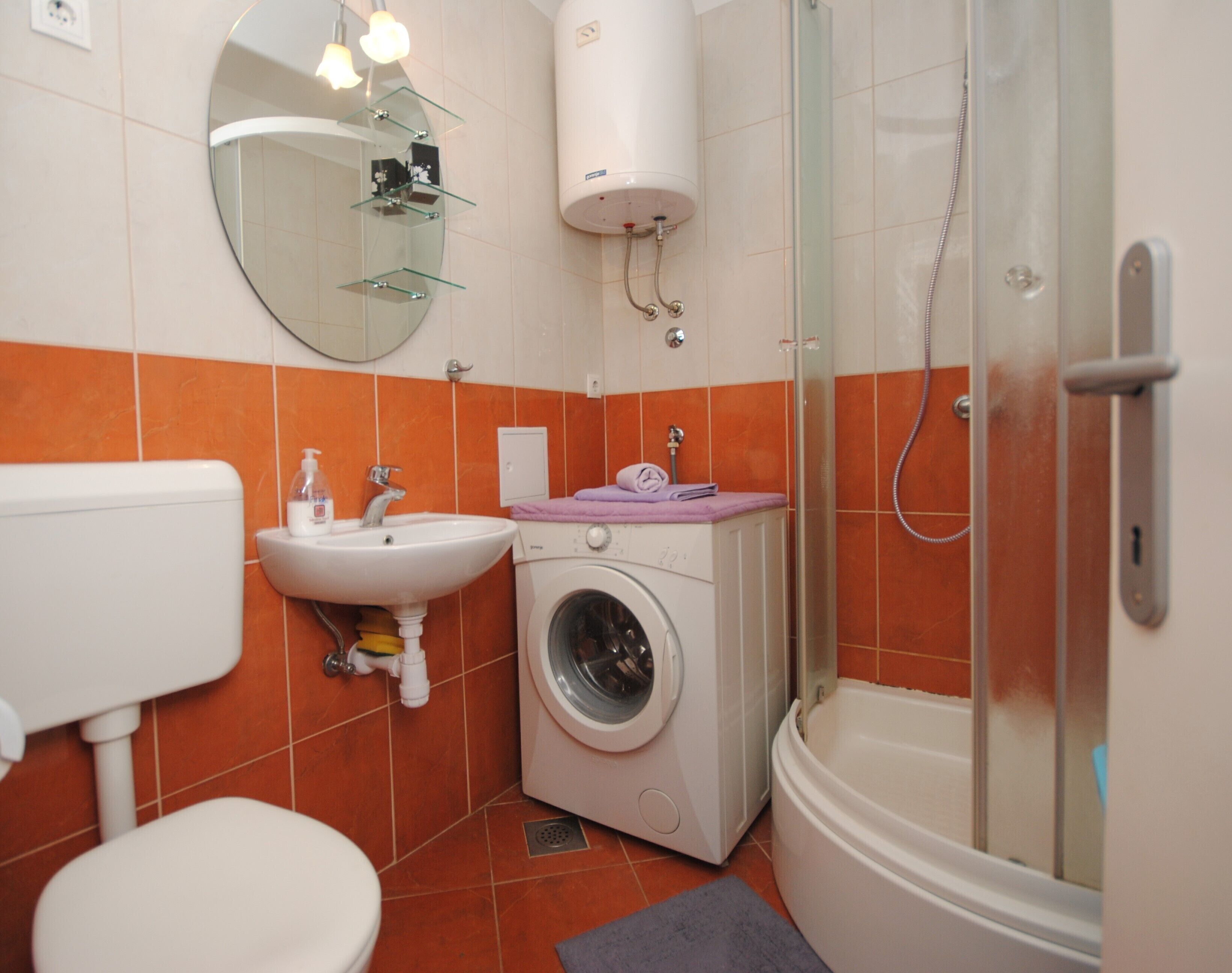Une petite salle de bain comprenant des toilettes, un lavabo, un lave-linge et une douche.