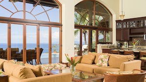 A spacious living area with a large glass door leading to a balcony overlooking the ocean, a cozy seating arrangement, and a kitchen area with dark wooden cabinets. - Cinco Sinsotes (Sardinal)