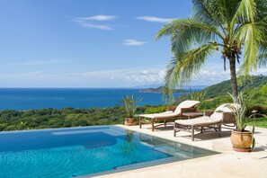 An infinity pool with a clear view of the ocean and hills. There are lounge chairs and potted plants. - Cinco Sinsotes (Sardinal)