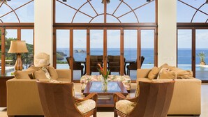 A spacious living area with a large window overlooking the ocean, featuring a sofa, two armchairs, and a coffee table. - Cinco Sinsotes (Sardinal)