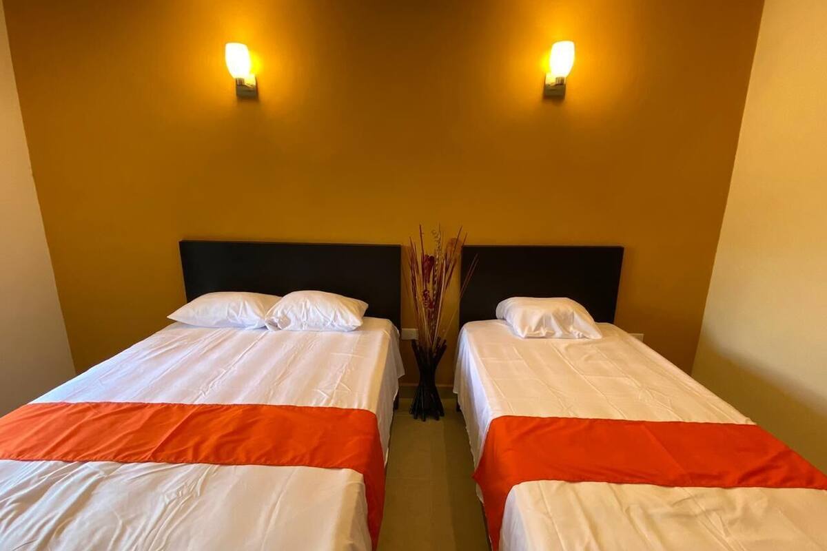 A hotel room with two beds, each with white bedding and orange accents, and a dark headboard.
