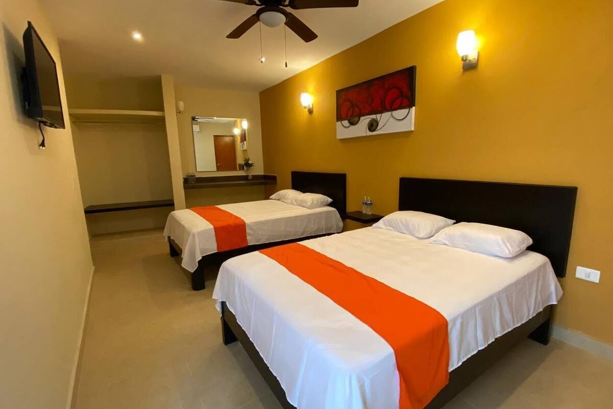 A hotel room with two beds, a ceiling fan, a TV, and a painting on the wall.