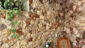 A corner room with a stone wall, two rocking chairs, a small table with a flower arrangement, and a shelf with plants. - Los Candiles (Valladolid)