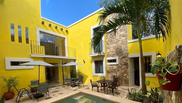 A yellow building with a swimming pool, outdoor seating, and potted plants. - Los Candiles (Valladolid)