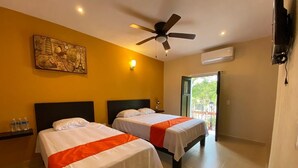 A hotel room with two beds, a ceiling fan, an air conditioning unit, and a window with a view of greenery. - Los Candiles (Valladolid)