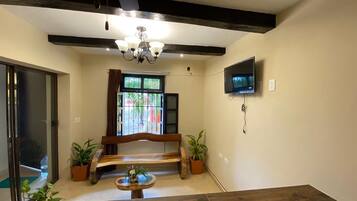 A living room with a wooden bench, a TV mounted on the wall, and a ceiling fan.