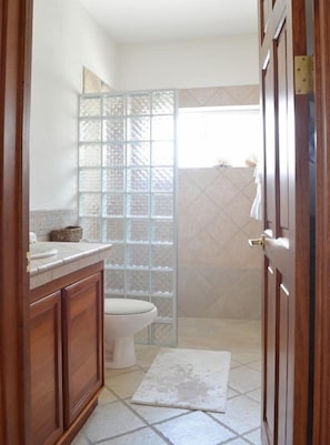 A bathroom with a wooden vanity, a toilet, and a glass shower enclosure. - Casa Oso Grande (Sardinal)
