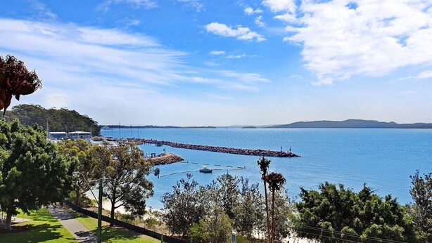 A coastal view with a pier extending into the water, surrounded by greenery and a clear sky. - Kiah 10, 53 Victoria Parade - Stunning Views, Aircon and Close to the Marina (Nelson Bay)