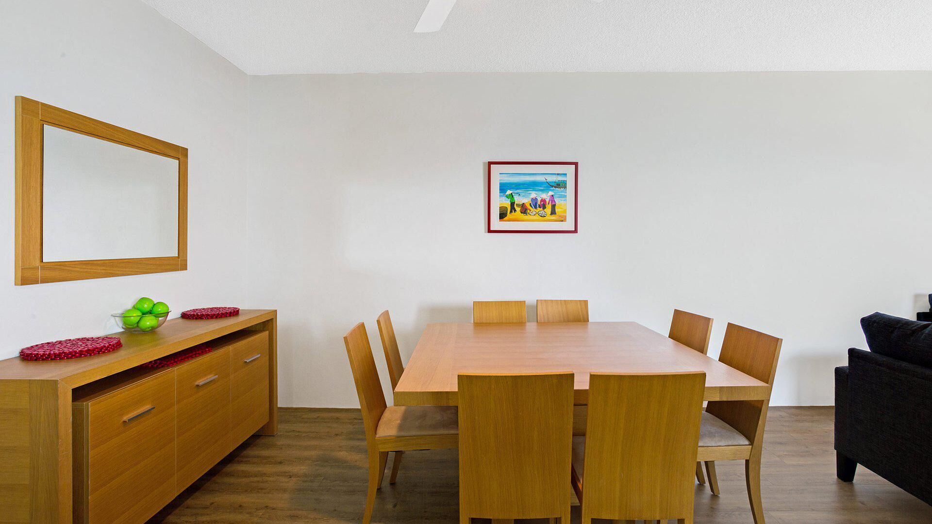 Un comedor con una mesa y sillas de madera, un armario de madera con cajones y un cuadro enmarcado en la pared.