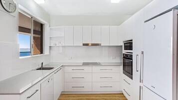 Una cocina moderna con armarios blancos, un lavamanos de acero inoxidable y un horno empotrado.