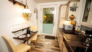 Une cuisine compacte avec un coin repas, un plancher en bois et une vue à travers la porte vitrée.