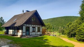 Une maison traditionnelle à colombages, dotée d’un toit en pente, d’un petit porche et offrant une vue sur une colline boisée.