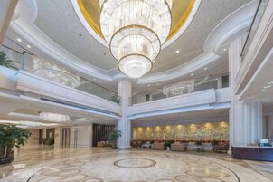 Un hall de hotel de varios niveles con una imponente lámpara de araña, una recepción y un suelo de mármol circular.