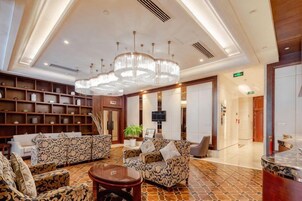Un vestíbulo amplio con techo alto, un candelabro, un mostrador de recepción y una zona de estar con sofás estampados.