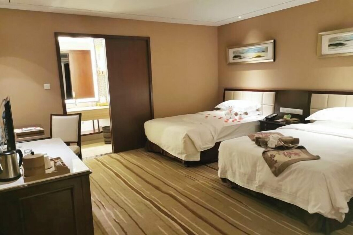 Habitación de hotel con dos camas, un escritorio con silla y un ventanal grande.