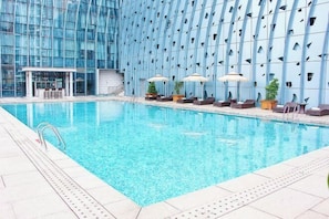 Una piscina interior con pared de vidrio moderna, sillas de descanso y sombrillas.