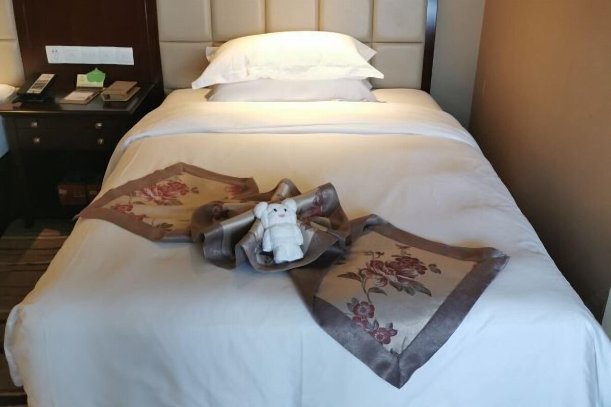 A neatly made bed with a floral pillow and a small stuffed animal.