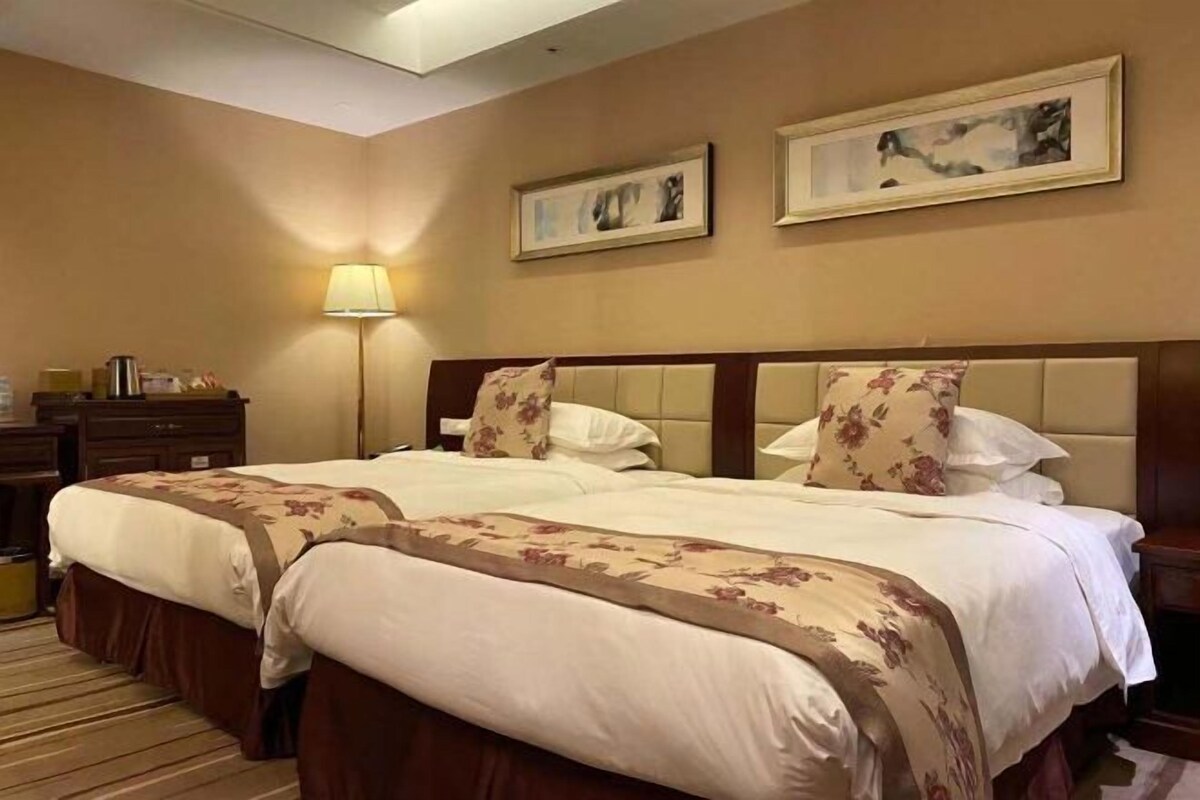 Habitación de hotel con dos camas, una mesita de noche, una lámpara y dos cuadros en la pared.