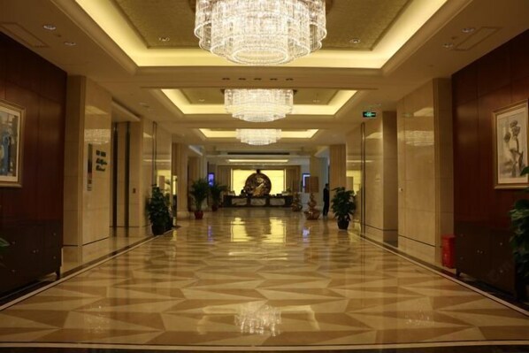 A spacious lobby with a polished floor, large chandeliers, and potted plants.