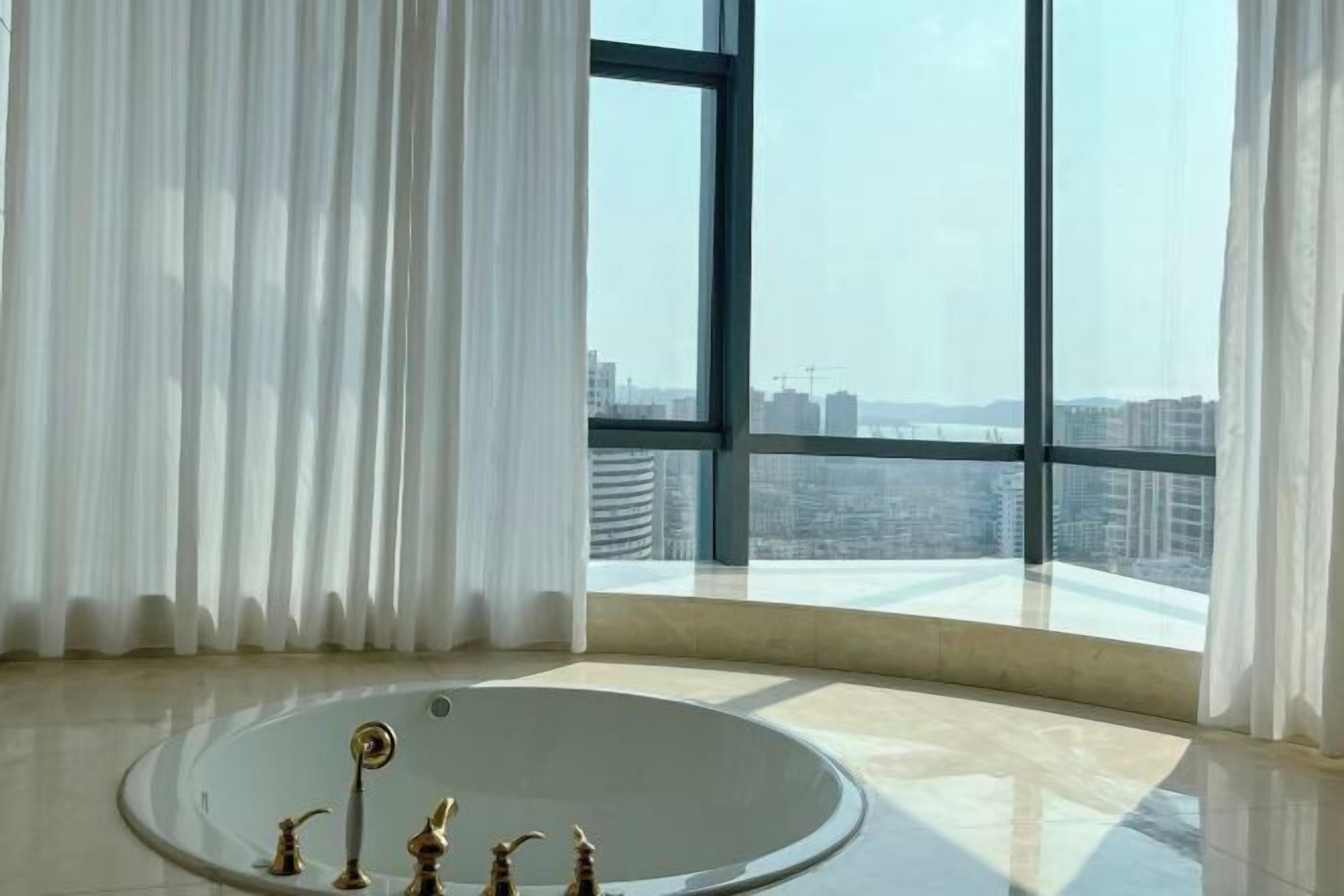 Un bagno moderno con una vasca da bagno ampia, vista sulla città attraverso ampie finestre e una tenda.
