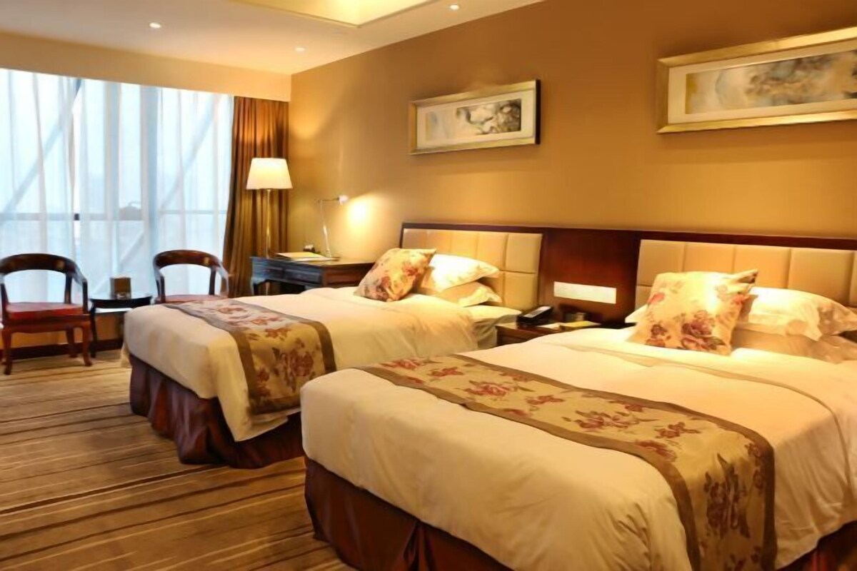 Habitación de hotel con dos camas, un escritorio, una silla y ventanas amplias.