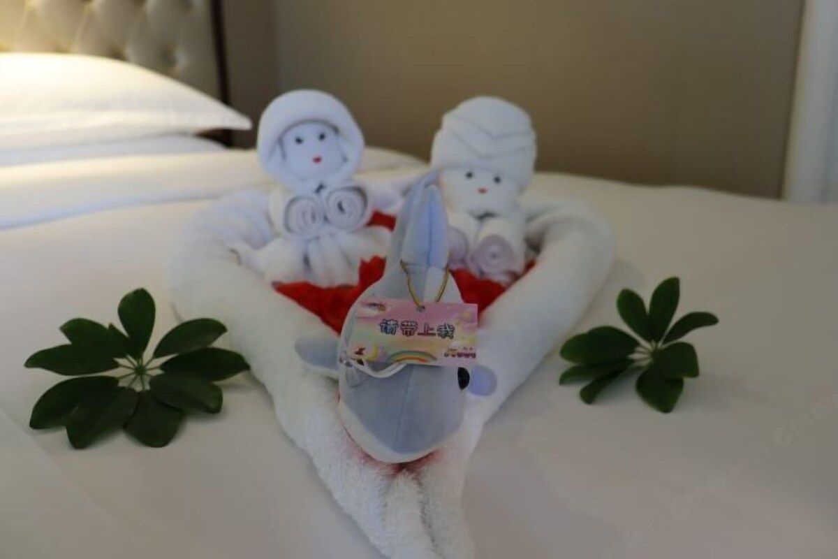 A bed with a towel shaped like a horse head, two plush toys, and a small tag.