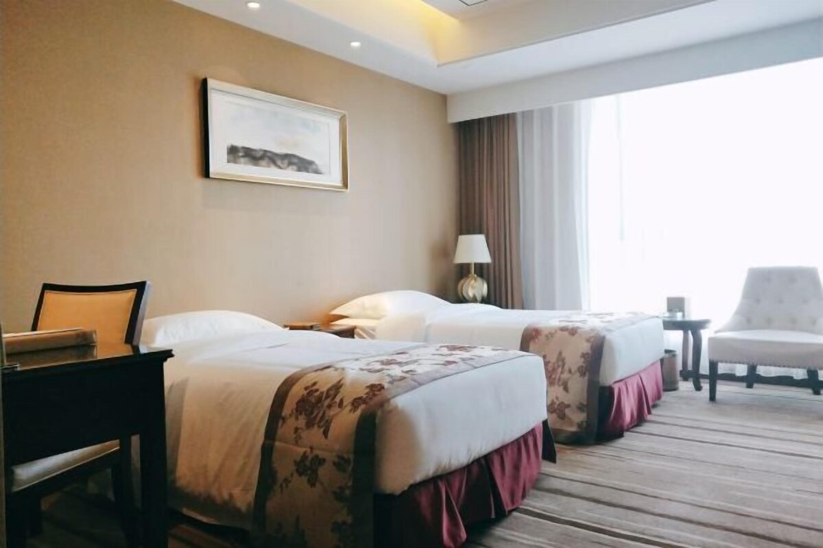 Una habitación de hotel con dos camas, un escritorio, una silla, una lámpara y una ventana con cortinas.