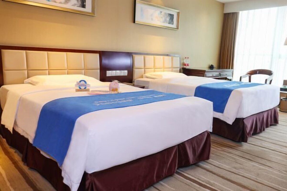 Una habitación de hotel con dos camas, cada una con cubrecama azul y blanco, cabecero de madera y un escritorio con silla.