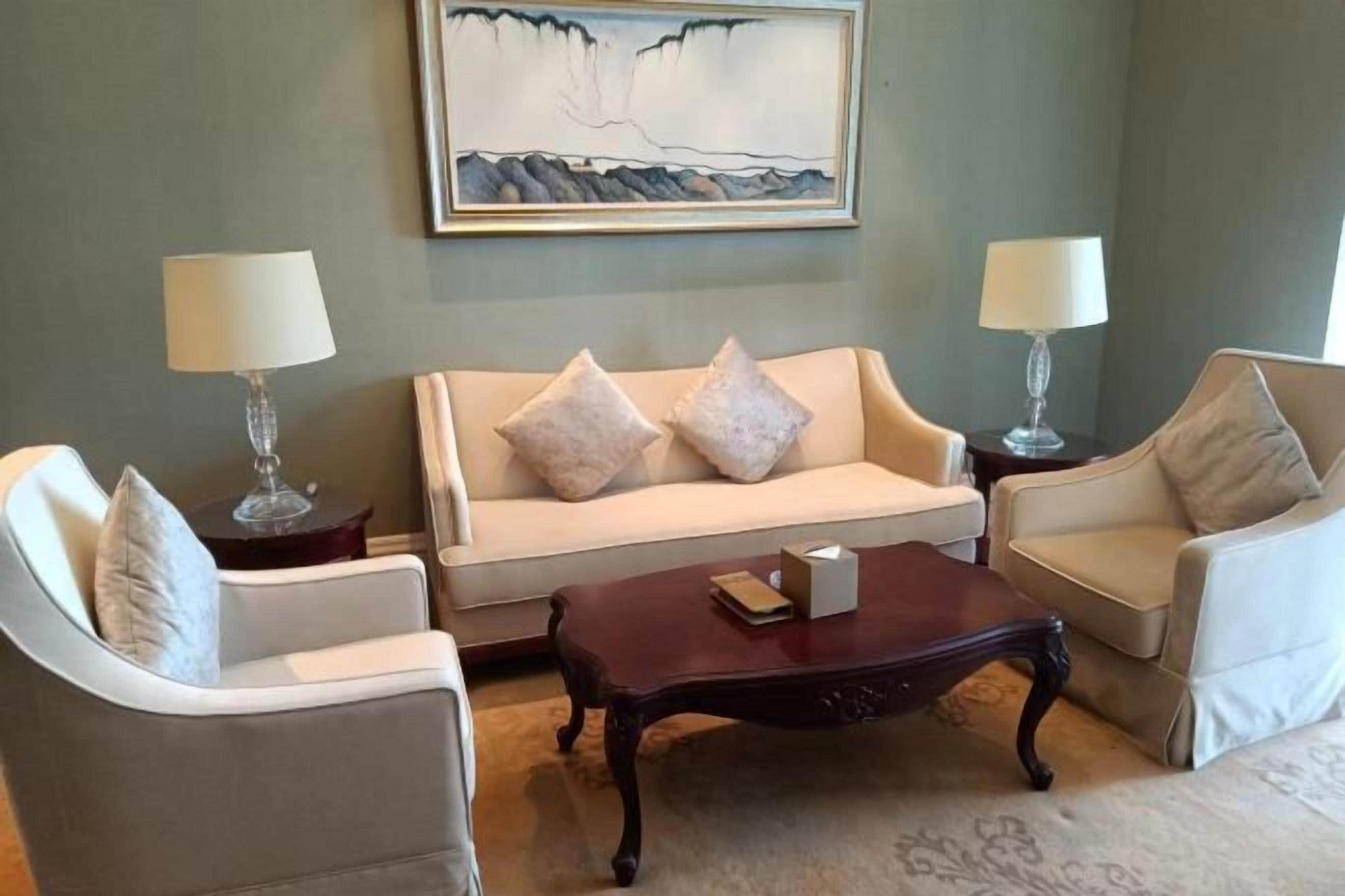 A living room with a beige sofa, two armchairs, a coffee table, and two lamps.