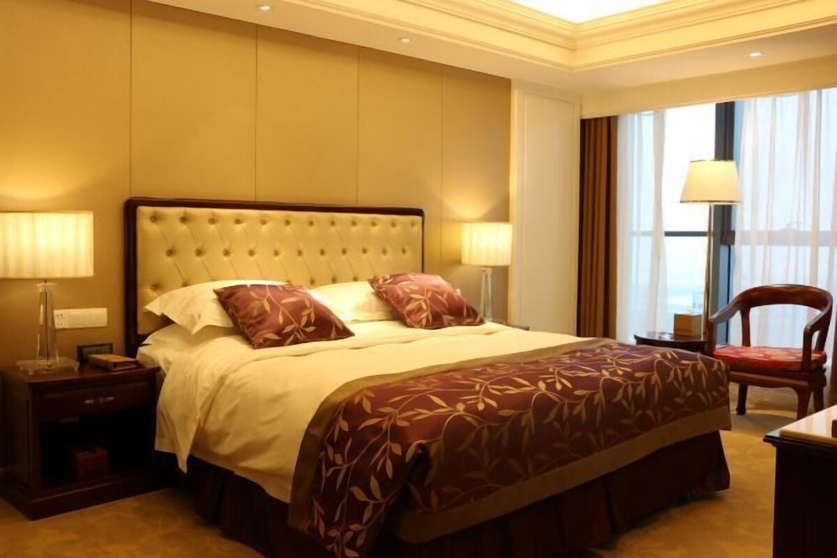 Habitación de hotel con una cama grande, dos mesitas de noche con lámparas, una silla y vistas al exterior a través de una ventana.
