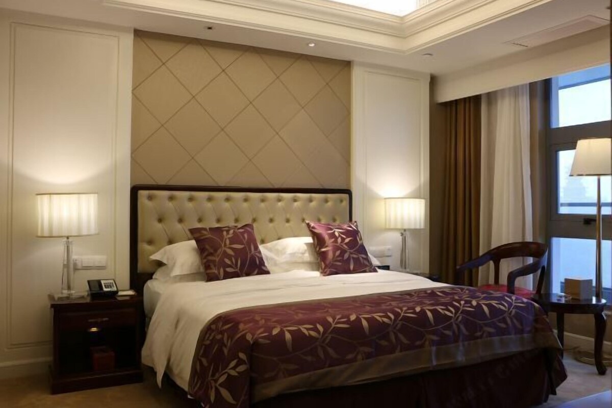 Una habitación de hotel con una cama grande, dos mesitas de noche, una silla y una ventana con cortinas.