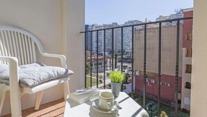 Un balcon avec une chaise blanche, une petite table sur laquelle se trouvent une tasse et une plante, et une vue sur les bâtiments environnants.