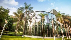 A modern building with a curved glass facade surrounded by palm trees and greenery. - Minjiang Donghu Hotel (Meishan)