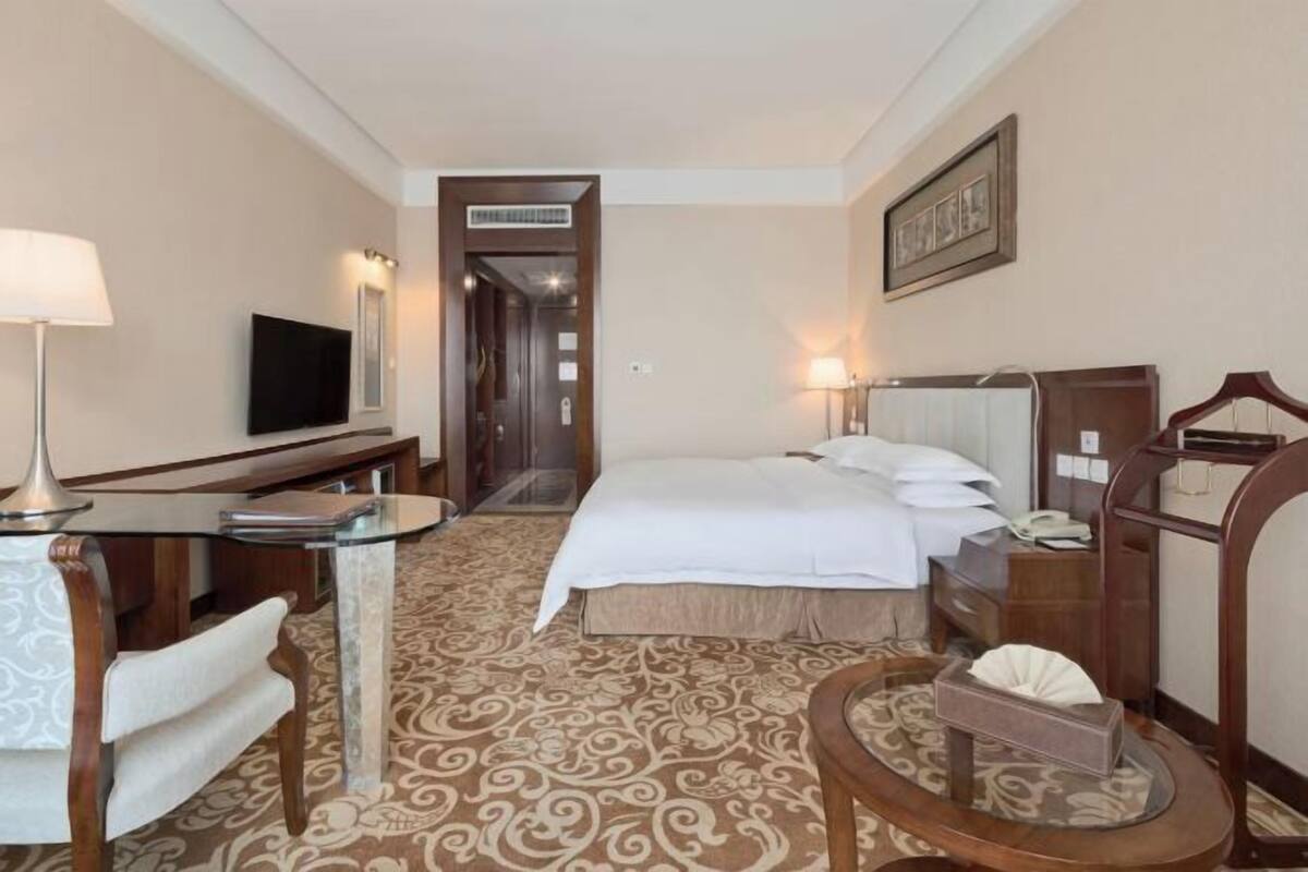 A hotel room with a bed, bedside table, lamp, chair, and a television.
