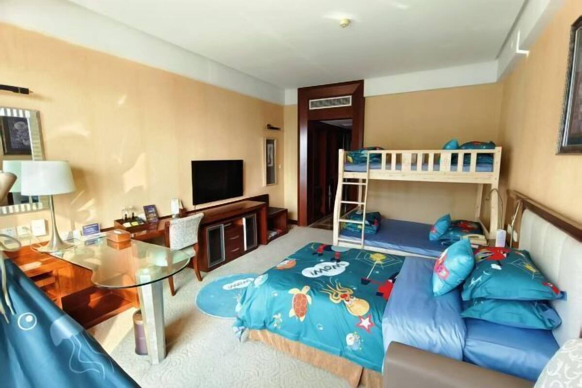 A compact room with a bunk bed, a desk with a computer, a television, and a glass table.