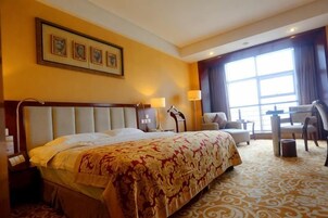 Habitación de hotel con una cama grande, un escritorio y una silla. Hay una ventana con cortinas, una lámpara y un cuadro en la pared.