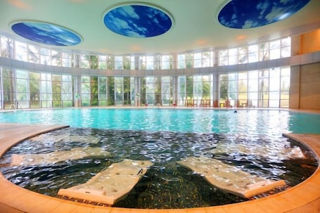 A large indoor swimming pool with a hot tub, surrounded by large windows and a circular ceiling design.. Minjiang Donghu Hotel